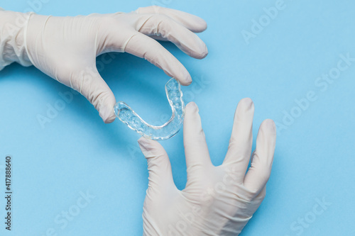 Bild auf Leinwand Hands of a dentist holding a transparent orthodontic with a blue background