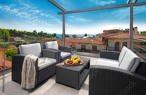 Recreation concept panorama of modern patio with wicker grey rattan furniture. Contemporary armchairs, couch, table on roof top terrace of luxury sea view resort in old European city