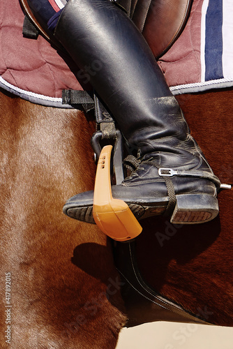 Close up black leather riding boots in stirrups on brown horse, copy space. Equestrian sport. Leg of the rider in the stirrup