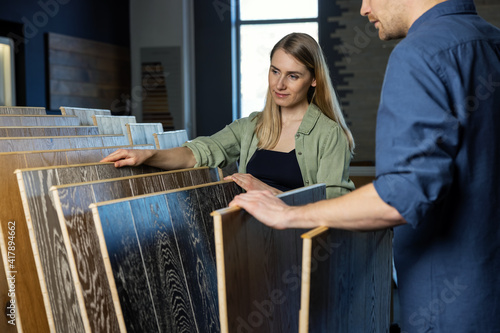 Valokuvatapetti young couple choosing wood texture laminate floor from samples in flooring store