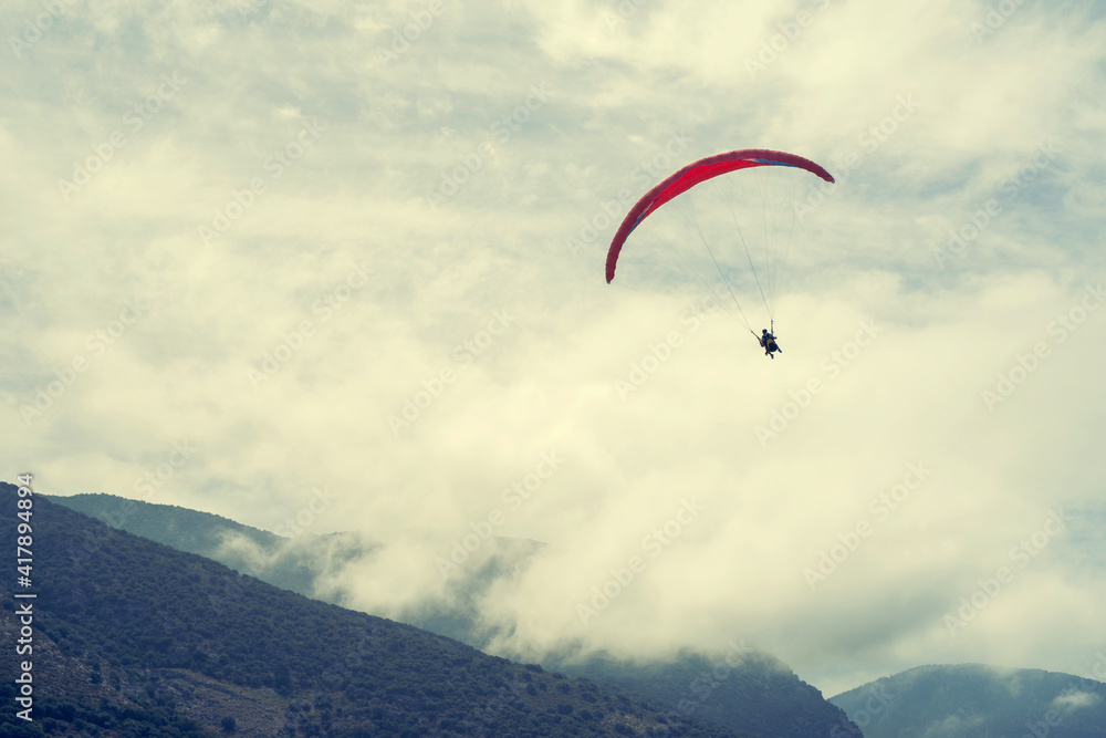 Athlete paragliding against the backdrop of a cloudy sky over the mountains Athlete paragliding against the backdrop of a cloudy sky over the mountains
