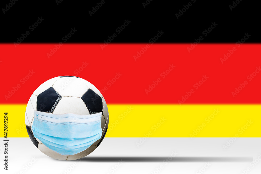 Soccer ball in a medical mask against the background of the flag of germany. Corona protection against viruses bacteria stop. Cancellation of sporting events. Copy space Soccer ball in a medical mask against the background of the flag of germany. Corona protection against viruses bacteria stop. Cancellation of sporting events. Copy space