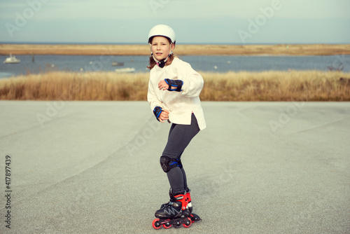 Fototapeta Happy child girl in white helmet, inline skates and safety equipment having fun