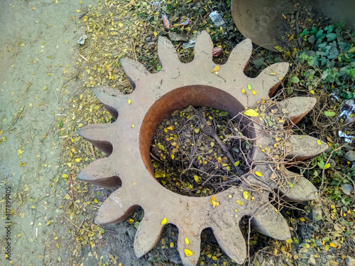 an old rustic big size gear surrounded by yellow and green leaf in a scrap yard of an old mill