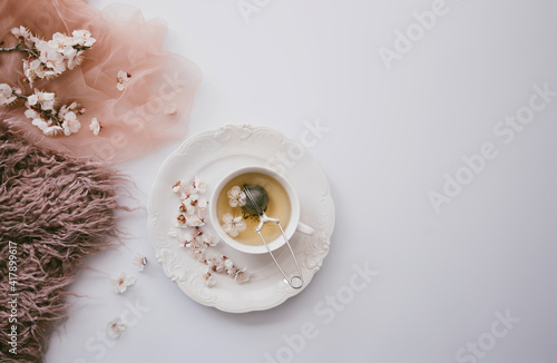 A cup of tea with apple tree blossom. Herbal tea in a white cup on a white wooden table with flowers. Tea ceremony. Copy space. Selective focus.