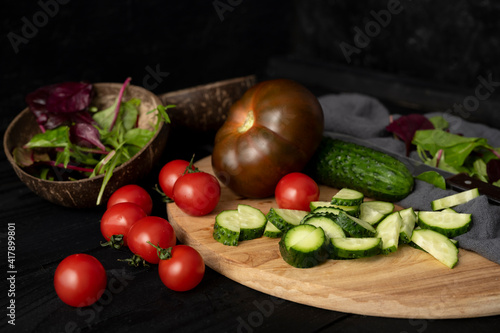 Ingredients for making salad on rustic black board background. Vegetable salad in bowl, tomato, cucumber, tomatoes kumato. Healthy, clean eating concept. Vegan or gluten free diet
