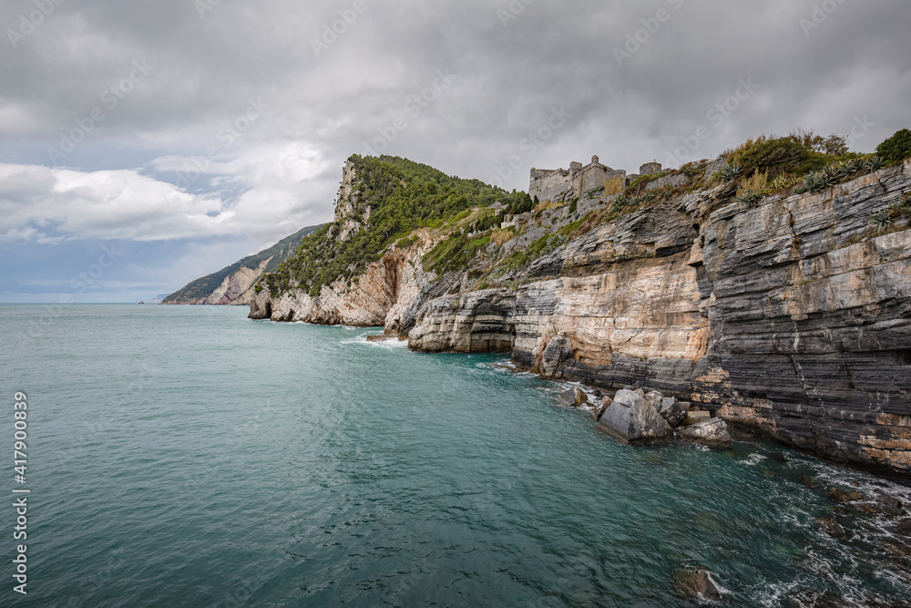 Beautiful seascape. Stormy sea on a windy day: blue waves breaks on the stone shore of Porto Venere with Doria Castle (12th century) on the top of mountain