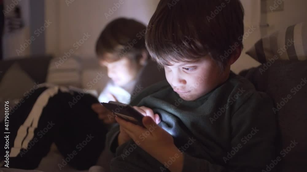 Caucasian boy playing video games on smartphone at home. His big brother playing on the blurry background Caucasian boy playing video games on smartphone at home. His big brother playing on the blurry background
