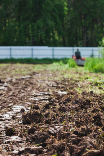 A man on a track cultivator digs a private plot. Focus on the foreground on clods of earth