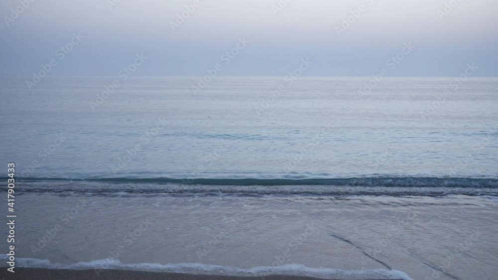 Calm blue sea waves on the sandy beach and the morning horizon in the distance Calm blue sea waves on the sandy beach and the morning horizon in the distance