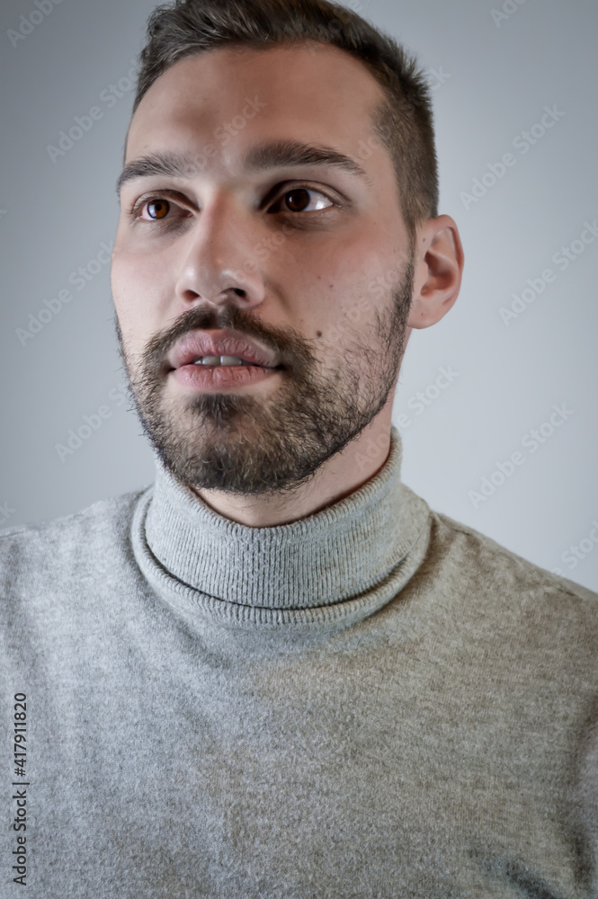 Fototapeta premium Portrait of a young brown-haired man with a short beard and a gray turtleneck sweater 