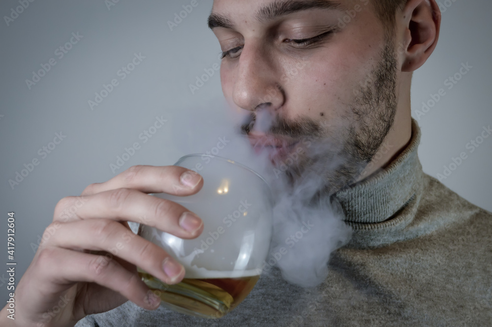 Portrait of a young bearded man exhaling smoke from an electronic cigarette holding a glass of beer close up Portrait of a young bearded man exhaling smoke from an electronic cigarette holding a glass of beer close up