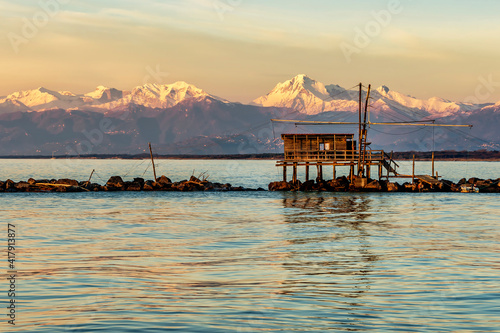 Trebuchet fishing hut at sunset, against the Alps covered with snow, Marina di Pisa, Tuscany, Italy