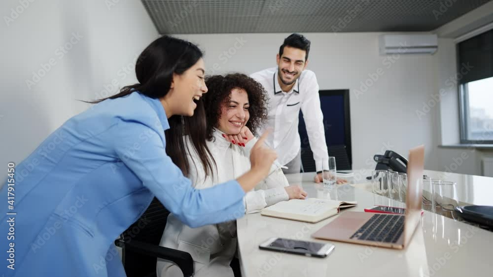 Portrait of smiling beautiful Caucasian woman sitting at conference table with laptop as Asian colleague talking and Middle Eastern coworker gesturing. Multiethnic team discussing success of startup. Portrait of smiling beautiful Caucasian woman sitting at conference table with laptop as Asian colleague talking and Middle Eastern coworker gesturing. Multiethnic team discussing success of startup.