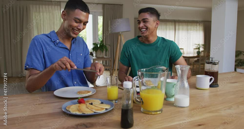 Happy mixed race gay male couple having pancakes for breakfast and laughing in kitchen Happy mixed race gay male couple having pancakes for breakfast and laughing in kitchen