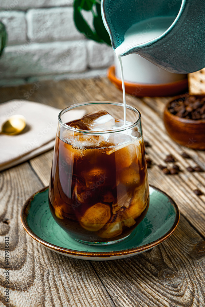 Cream is poured into a glass of iced coffee, vertical photo Cream is poured into a glass of iced coffee, vertical photo