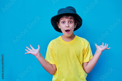 Portrait of boy with surprised face in yellow t-shirt, on blue background. Copy space