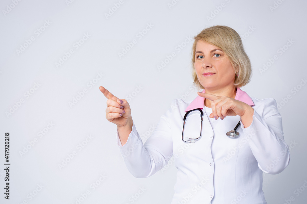 Mature female caucasian doctor pointing away forefinger, looking serious to camera. Empty side space for your health care advertisement.Informative concept Mature female caucasian doctor pointing away forefinger, looking serious to camera. Empty side space for your health care advertisement.Informative concept