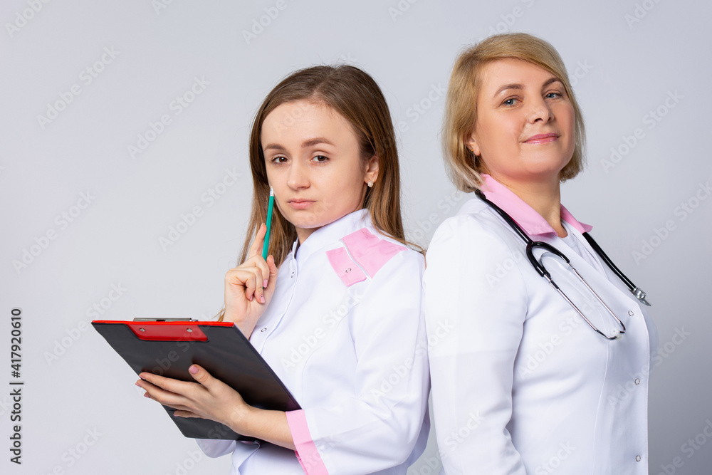 Serious surgeon team of doctors having a meeting at hospital. Thoughtfully pretty female practitioners with clipboard looking at camera on white background Serious surgeon team of doctors having a meeting at hospital. Thoughtfully pretty female practitioners with clipboard looking at camera on white background