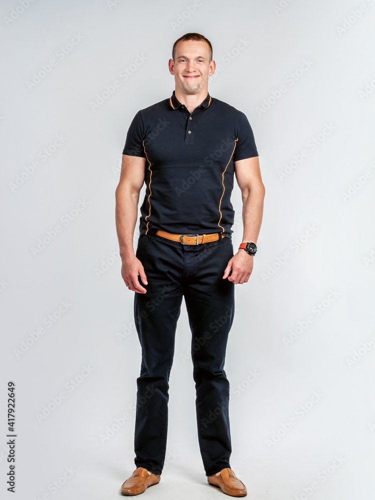 Fototapeta premium Full-length portrait of a man. A brutal man smiles at the camera. A man in black clothes. A person on a white background.