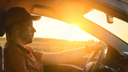 Caucasian Man in automobile in the countryside and sun rays. Male driver driving a car at sunset background. Summer travel, road trip and vacations concept. Side view