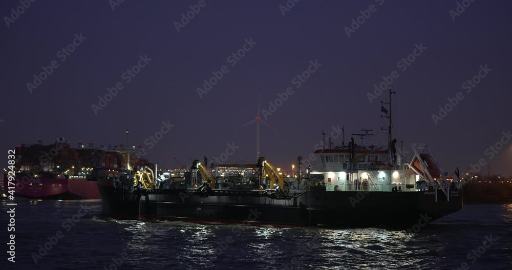 Hamburg, Hamburg, Germany, 02.25.2021 The suction Dredger Ijsseldelta is preparing to dredging the river elbe in the harbor of Hamburg at night. In background the container ship One Crane is seen. Hamburg, Hamburg, Germany, 02.25.2021 The suction Dredger Ijsseldelta is preparing to dredging the river elbe in the harbor of Hamburg at night. In background the container ship One Crane is seen.