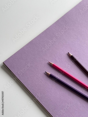 Colored pencils on purple paper album on white table. Artist, art and hobby. Drawing and painting