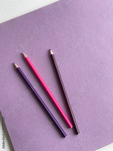 Colored pencils on purple paper album on white table. Artist, art and hobby. Drawing and painting