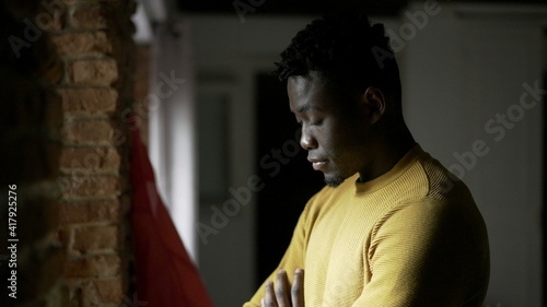 Pensive black African man standing by window, close-up face thinking