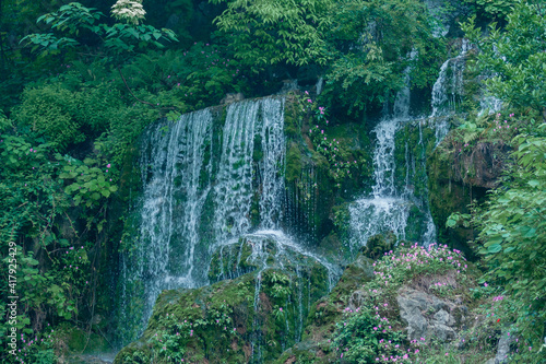 Guilin, China - May 11, 2010: Seven Star Park. Tall waterfall with mulitple white water streams over rocks grown with green plants, trees, and pink flowers. photo