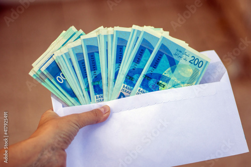 Fotografija A hand holding envelope with many israeli 200 shekel banknotes