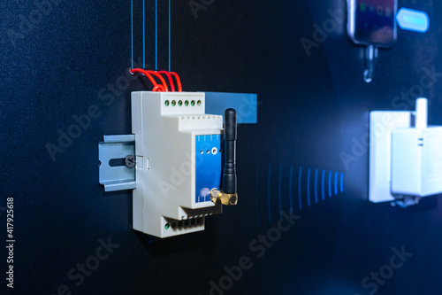 Radio relay unit is fixed to a DIN rail on a dark wall. Wireless power supply control unit. Device for closing / opening an electrical circuit. Demonstration of radio relay unit. Power supply concept. photo