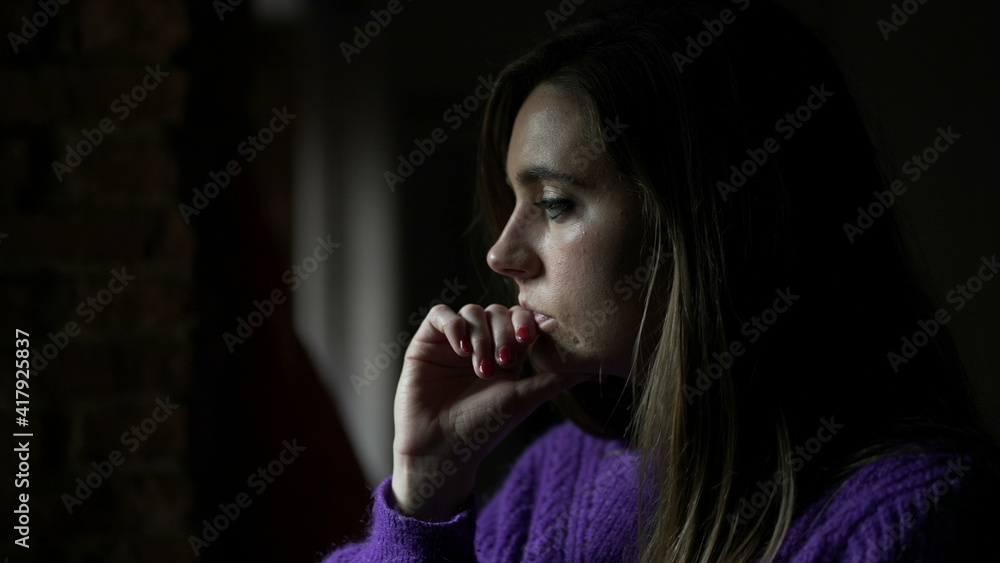 Thoughtful young woman standing by window thinking about life looking outside indoors Thoughtful young woman standing by window thinking about life looking outside indoors