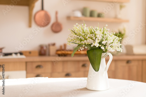 Bouquet of spring fragrant flowers of lilies of the valley in a vase on the kitchen table. Light Scandinavian style. Mother's Day. March 8, International Women's Day