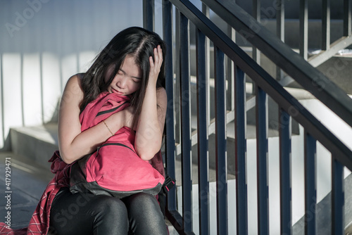 young depressed and scared Asian Chinese student girl suffering abuse and harassment at school victim of bullying and discrimination sitting on college staircase tormented © TheVisualsYouNeed