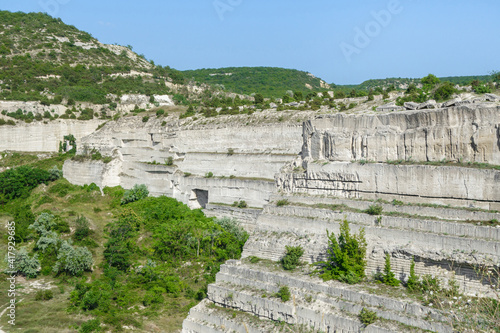 Snow-white steep slopes of an industrial quarry. The walls are riddled with traces of stone cutting. The height of the walls reaches 25-35 meters