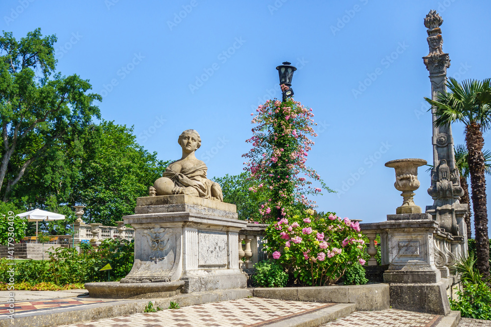 Panorama of old park decorations in Massandra palace. There are sphinx with female head, bowl & column in baroque style & lots of flowers. Shot near Yalta, Crimea