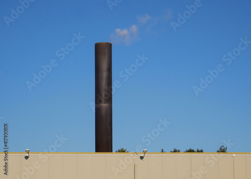 Smokestack of an active incinerator with white smoke and blue sky