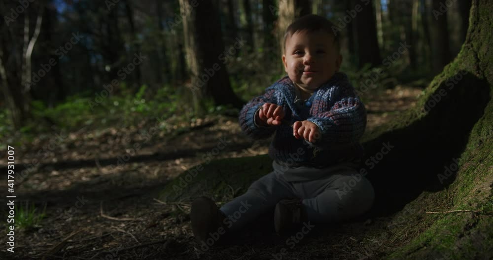 A little baby is sitting on the ground in the woods and is playing with a stick on a sunny spring day A little baby is sitting on the ground in the woods and is playing with a stick on a sunny spring day