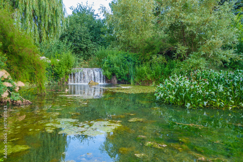 Panorama of lake with waterfall. Trees, bushes and water plants are guarding waters like natural solid wall. Shot in Vorontsov park (other names are Salgirka or Bagrov park), Simferopol, Crimea