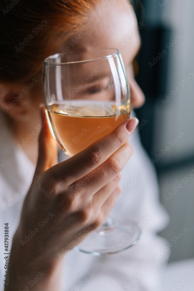 Close-up of attractive redhead young woman holding glass with champagne near face, looking away. Portrait of pretty female with glass of wine. Close-up of attractive redhead young woman holding glass with champagne near face, looking away. Portrait of pretty female with glass of wine.