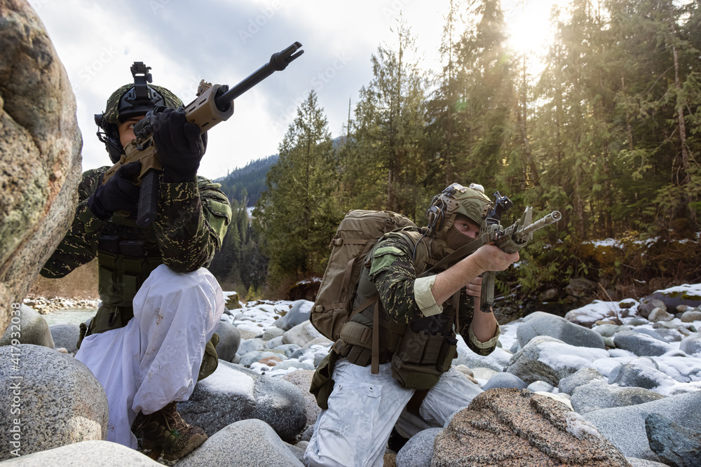 Fototapeta premium Army Man wearing Tactical Uniform and holding Machine gun in the Outdoor Rain Forest. Winter Warfare. Taken in British Columbia, Canada.