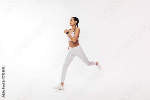 Fitness woman in sportswear running over white background in studio