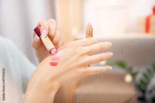 Woman is choosing new lipstick applies colour on skin of hand