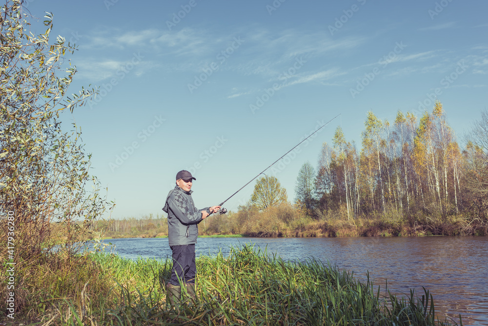 Man stands on the shore with a fishing rod. On a sunny day. Beautiful fishing landscape