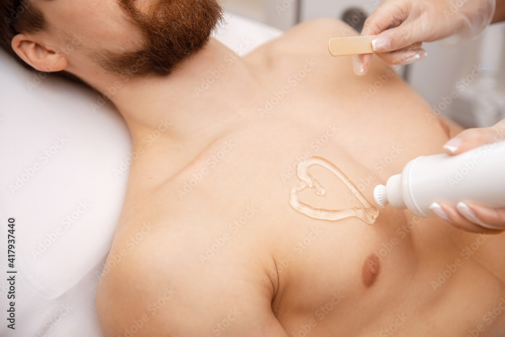 Naklejka premium Laser depilation concept for men. Beauty salon worker applies gel to guy body before hair removal