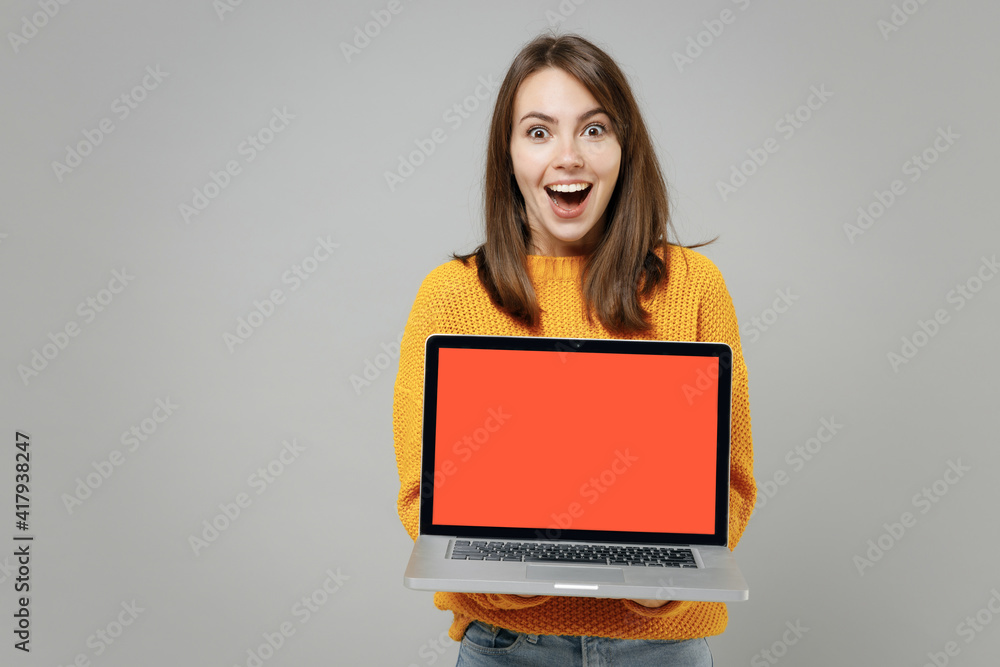 Naklejka premium Young smiling freelancer copywriter attractive caucasian woman 20s in knitted yellow sweater hold laptop pc computer with blank screen workspace area isolated on grey color background studio portrait