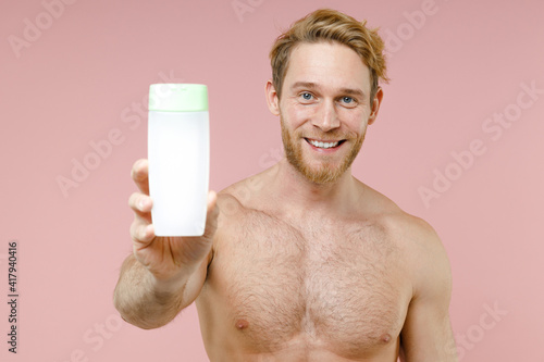 Cheerful bearded naked young man 20s perfect skin hold empty blank bottle of micelar water lotion tonic isolated on pink background studio portrait. Skin care healthcare cosmetic procedures concept. photo