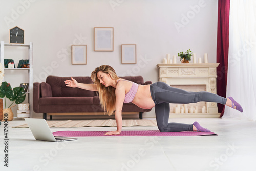 Happy attractive pregnant woman in sports clothes, doing exercises on the gym mat at home in the living room. health during pregnancy. yoga classes at home. Motherhood, active pregnancy.