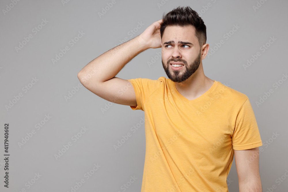 Young caucasian confused troubled thoughtful bearded pensive attractive handsome student man in casual yellow basic t-shirt sctratch back head look aside isolated on grey background studio portrait. Young caucasian confused troubled thoughtful bearded pensive attractive handsome student man in casual yellow basic t-shirt sctratch back head look aside isolated on grey background studio portrait.